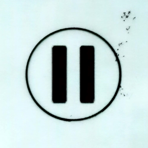 A black pause symbol, consisting of two vertical bars inside a thin circle, is centered on a light, slightly textured background with a few dark smudges in the upper-right corner
