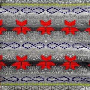 A grey knit fabric features a repeating pattern with rows of red geometric shapes resembling leaves, rows of blue infinity symbols, and subtle white snowflake motifs
